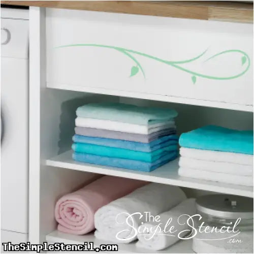 Close-up of a decorative branch flourish vinyl decal on a smooth white furniture surface.