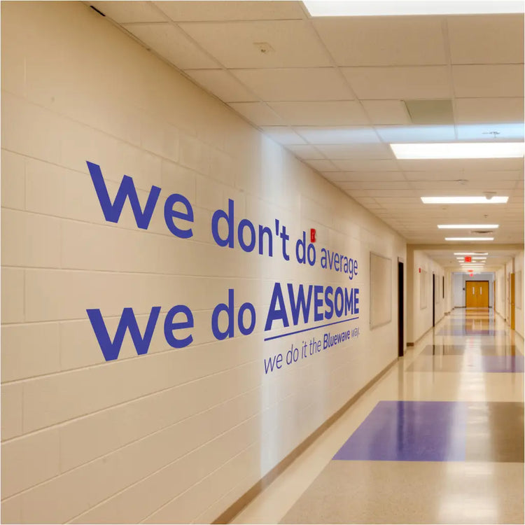 Large custom school wall decal reading "We Don't Do Average, We Do AWESOME The Bluewave WAY" in a modern, bold font on a bright school hallway wall, ideal for back-to-school decor.
