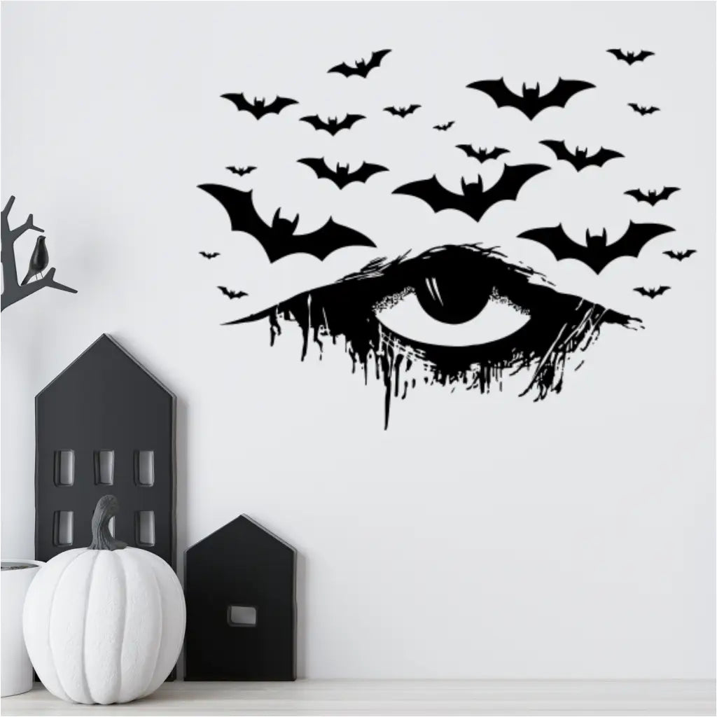 A black vinyl Halloween decal of a distressed, dripping eye with bats flying above it, applied to a white wall. The decal is surrounded by other stylish, minimalist Halloween decorations, creating an elegant and spooky scene for an interior.