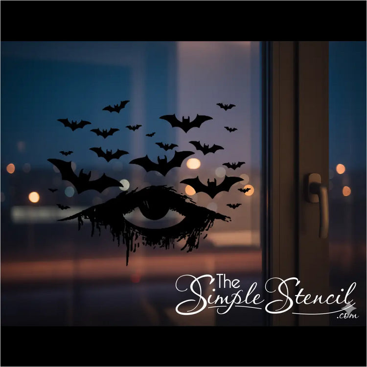 A black vinyl Halloween decal of a distressed, dripping eye with numerous bats flying above it, applied to a window at dusk. Blurred city lights are visible in the background, creating a moody and atmospheric gothic Halloween scene.