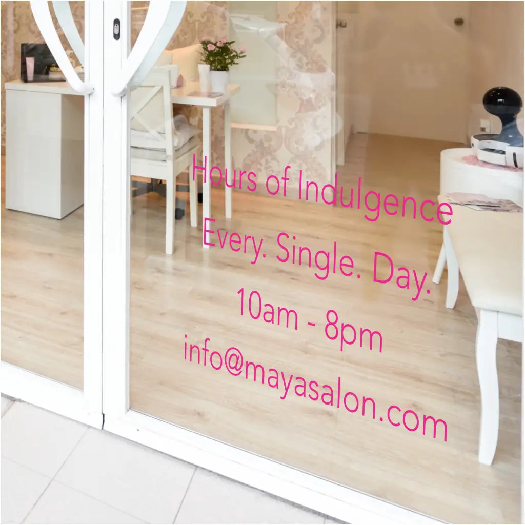 Chic salon window with a "Hours of Indulgence" decal and custom hours, complementing the elegant facade. By The Simple Stencil