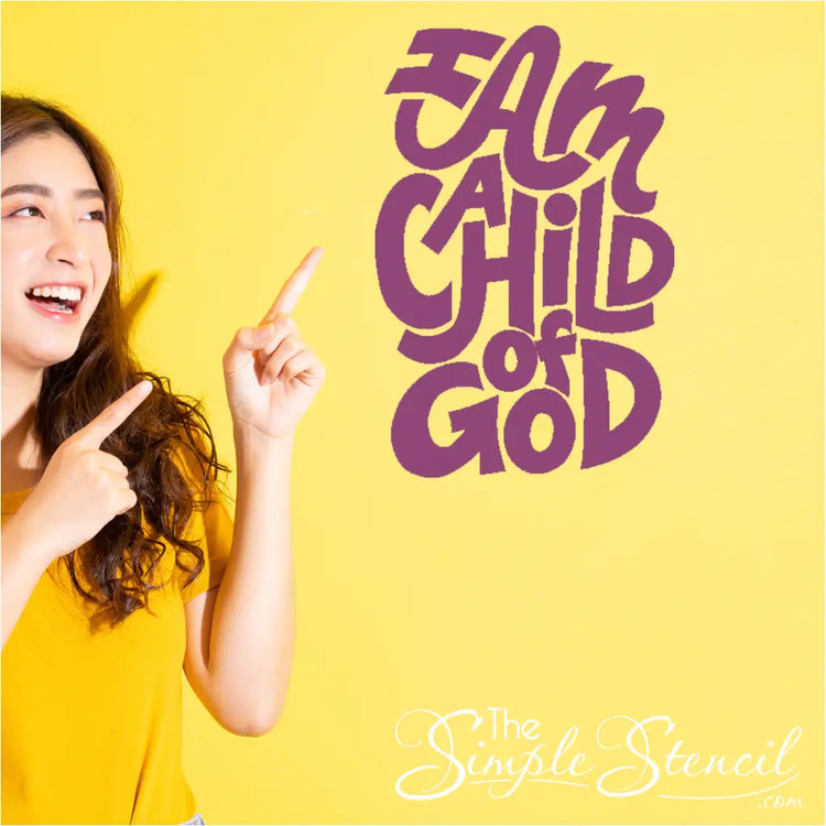 Smiling young teen pointing at  "I Am A Child of God" wall decal in a brightly lit church classroom wall. 