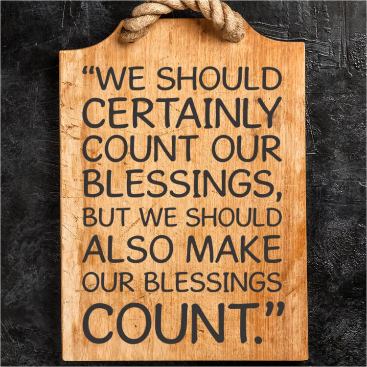 The Neal A. Maxwell quote "Make Our Blessings Count" displayed on a rustic wooden cutting board with a rope handle, set against a dark textured wall.