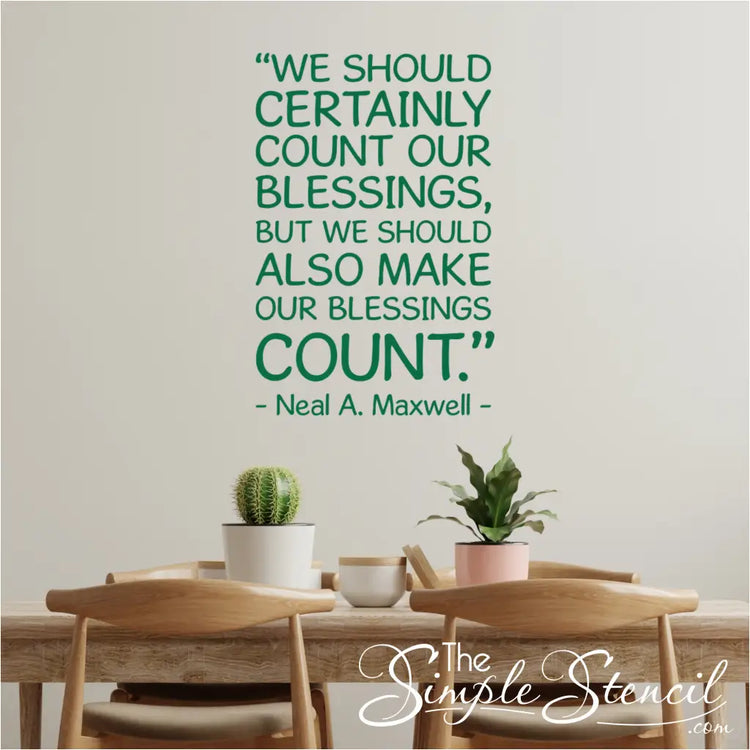 A green version of the Neal A. Maxwell "Make Your Blessings Count" decal shown on a wall in a modern dining room above a table with small plants.