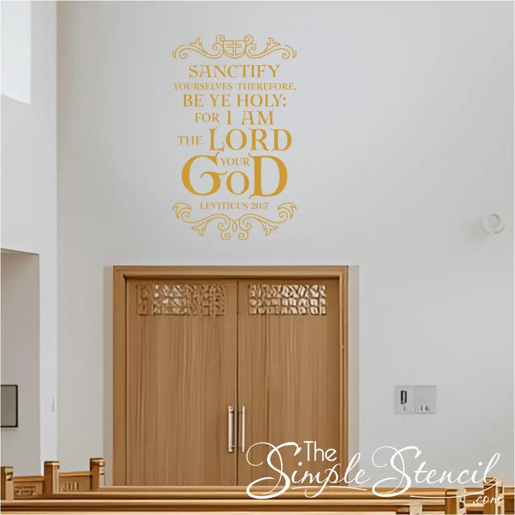 A golden Leviticus 20:7 Bible verse wall decal prominently displayed on a light wall above large wooden double doors in what appears to be a church or chapel setting, with pews visible in the foreground.