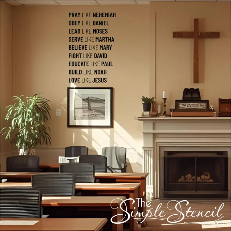 A black wall decal listing nine biblical virtues and figures, starting with "PRAY LIKE NEHEMIAH," installed on a beige wall in a room that appears to be a church classroom or lounge. A wooden cross hangs next to a fireplace, and several tables and chairs are visible.