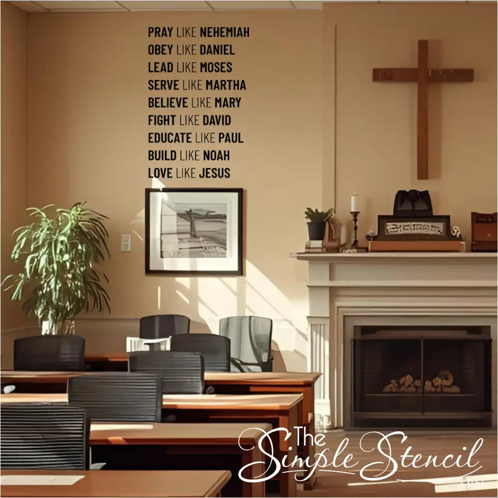 A black wall decal listing nine biblical virtues and figures, starting with "PRAY LIKE NEHEMIAH," installed on a beige wall in a room that appears to be a church classroom or lounge. A wooden cross hangs next to a fireplace, and several tables and chairs are visible.