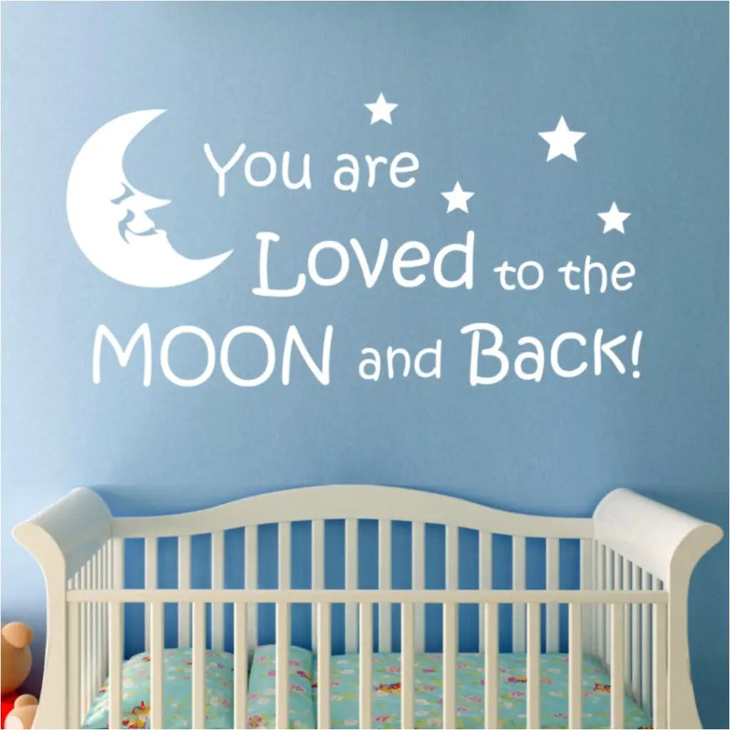 Large "You are loved to the moon and back" vinyl wall decal by The Simple Stencil displayed on blue baby nursery wall over crib.