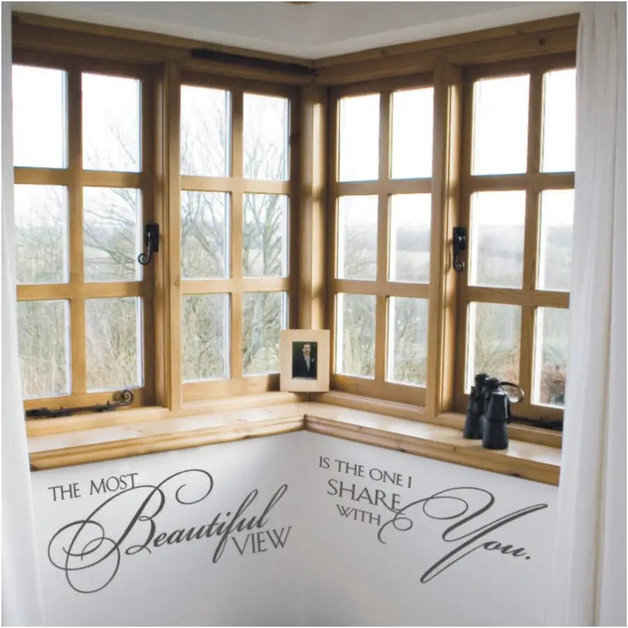 A large master bedroom corner window with a beautiful view adorned with a wall decal quote that reads: The most beautiful view is the one I share with you. Adds a romantic touch to any home decor project. 