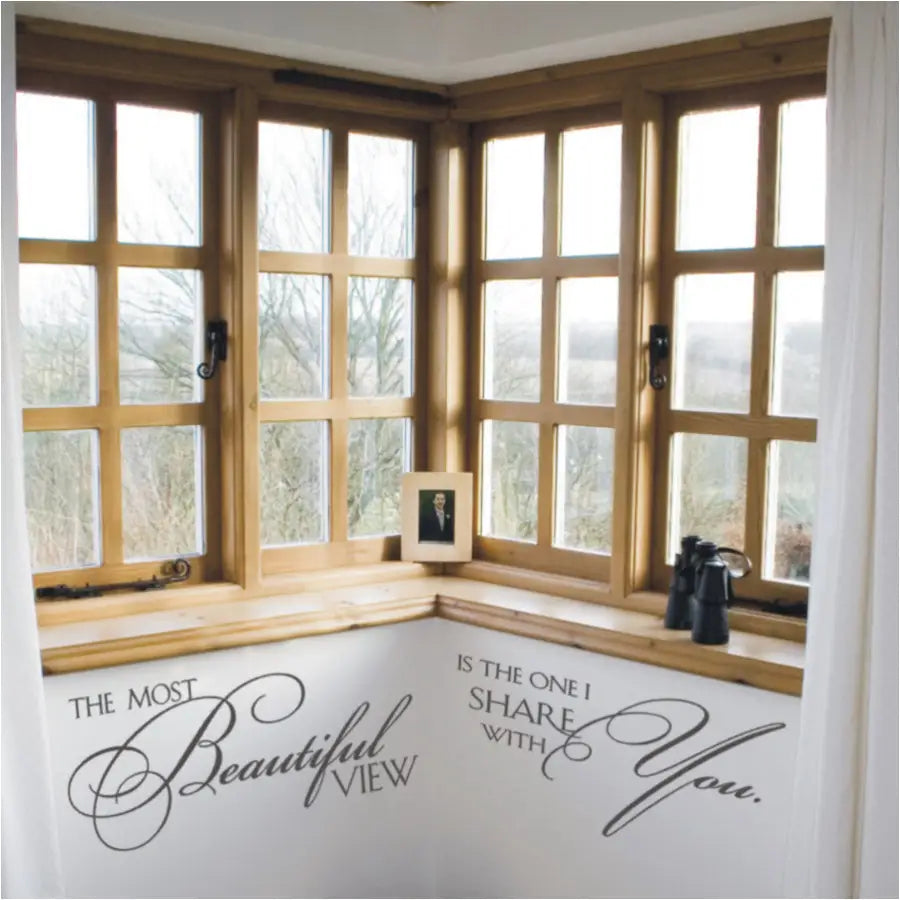 A large master bedroom corner window with a beautiful view adorned with a wall decal quote that reads: The most beautiful view is the one I share with you. Adds a romantic touch to any home decor project.