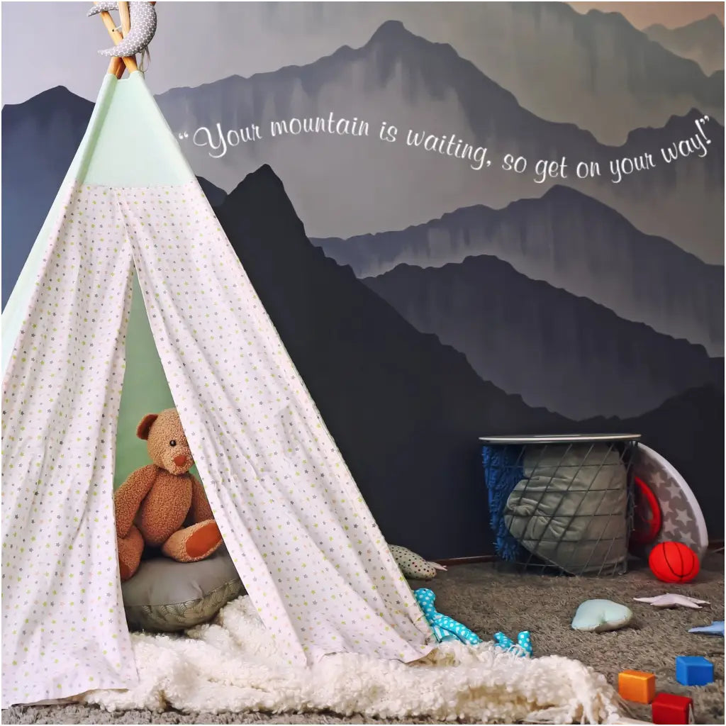 A super cute vinyl wall decal by The Simple Stencil on a boy's bedroom wall with mountain murals reads: Your mountain is waiting, so get on your way!