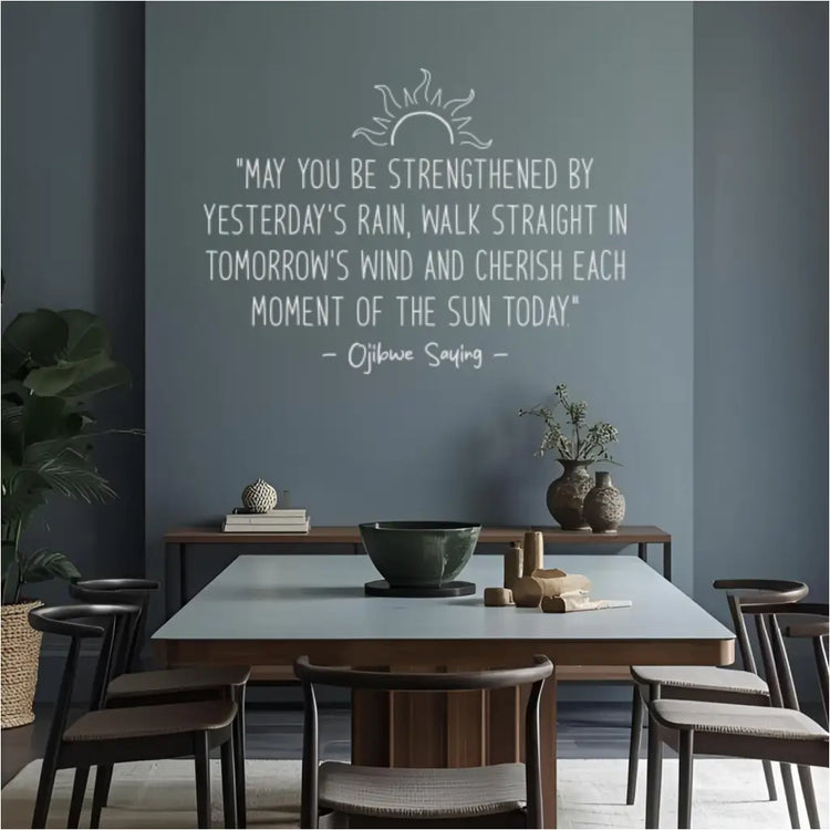 A white decal of the Ojibwe saying "Cherish each moment of the sun" on a dark blue statement wall in a modern, eclectic dining room.