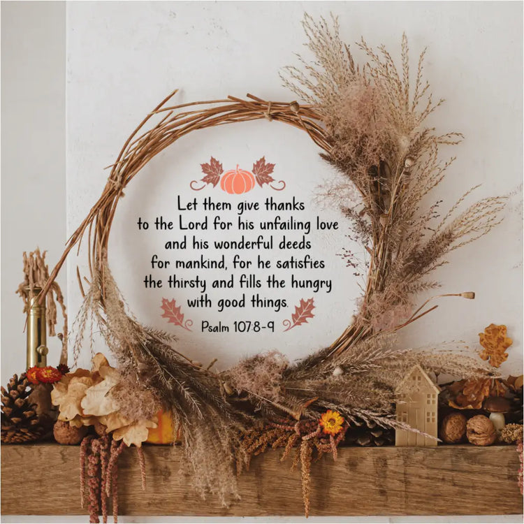 The Psalm 107:8-9 "Let them give thanks" wall decal is displayed inside a rustic grapevine wreath on a wooden fireplace mantel, surrounded by fall foliage and pinecones.