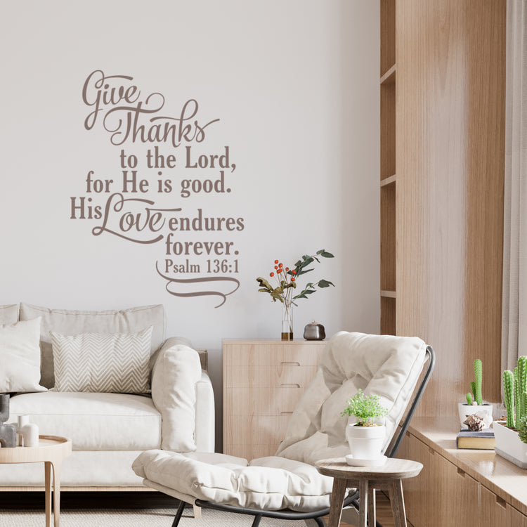 Scripture wall art sticker of Psalm 136:1 in a cozy living room with a light armchair, wood bookshelf, and modern, natural decor.