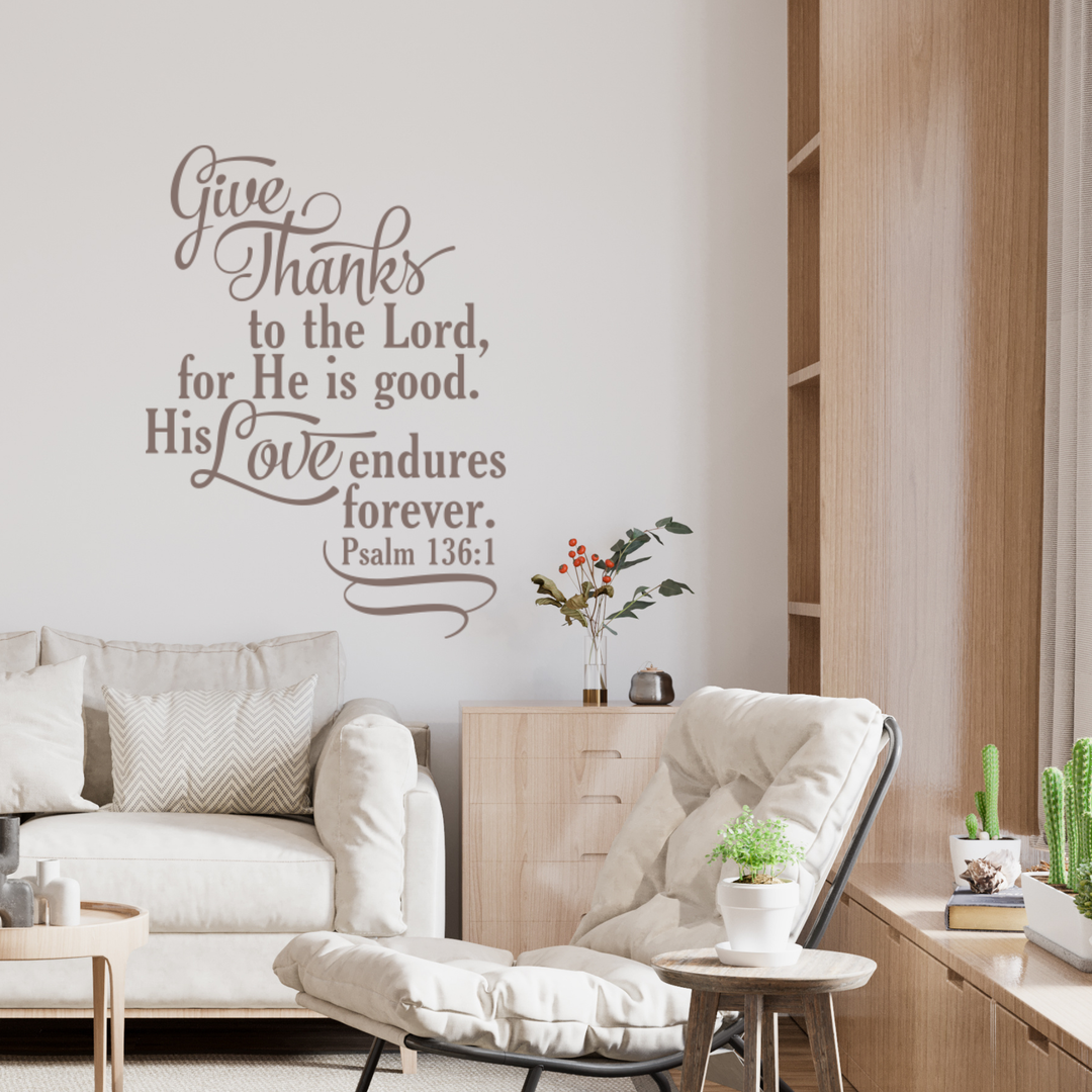 Scripture wall art sticker of Psalm 136:1 in a cozy living room with a light armchair, wood bookshelf, and modern, natural decor.