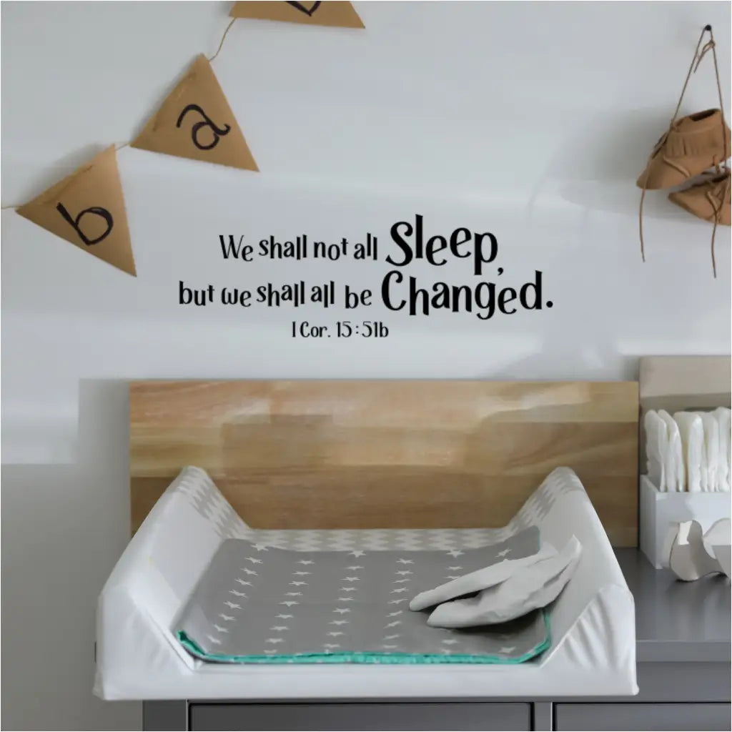 A humorous and thought-provoking wall decal reading "We shall not all sleep, but we shall all be changed. 1 Cor. 15:51b" positioned above a baby changing table in a nursery.