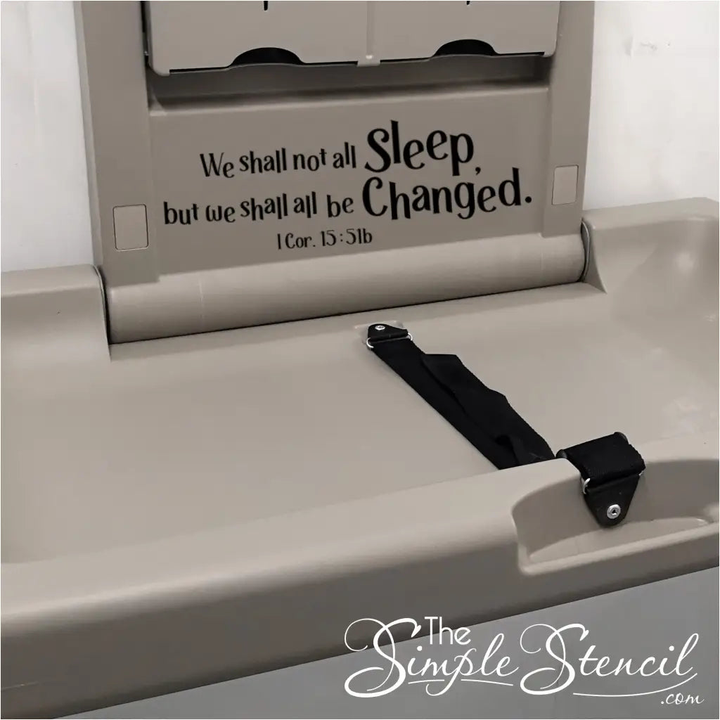 A lighthearted and relatable wall decal featuring "We shall not all sleep, but we shall all be changed. 1 Cor. 15:51b" above a diaper changing station in a church nursery.