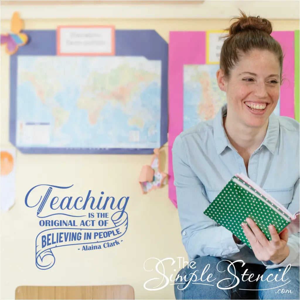 A teacher smiling in their classroom with the inspirational Alaina Clark quote decal visible in the background.