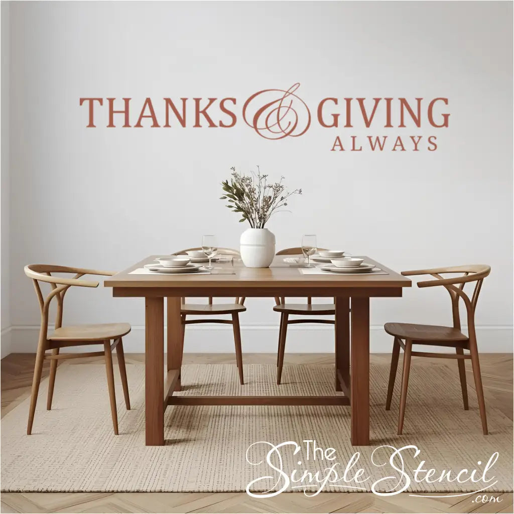 A warm, terracotta-colored 'Thanks and Giving Always' wall decal on the wall of a modern dining room above a wooden table set for a meal.