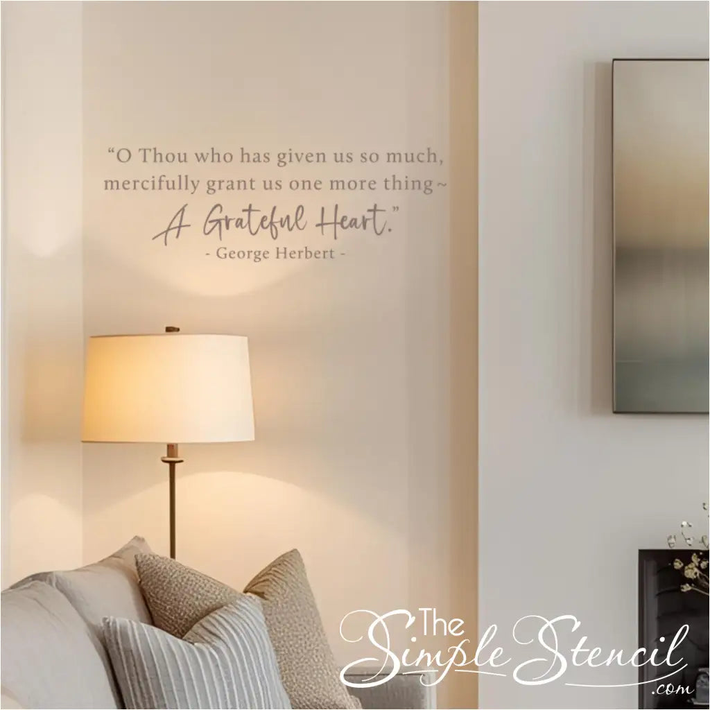 A subtle gray version of the George Herbert "A Grateful Heart" quote decal in a cozy living room corner above a sofa.