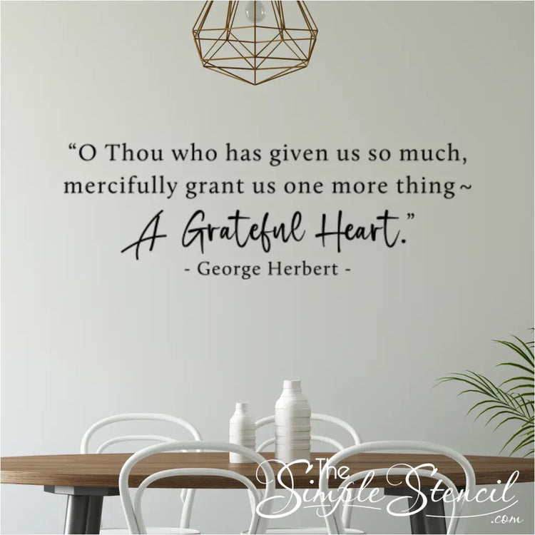 The George Herbert quote decal "A Grateful Heart" in black, displayed in a modern dining room with white chairs and a geometric light fixture.