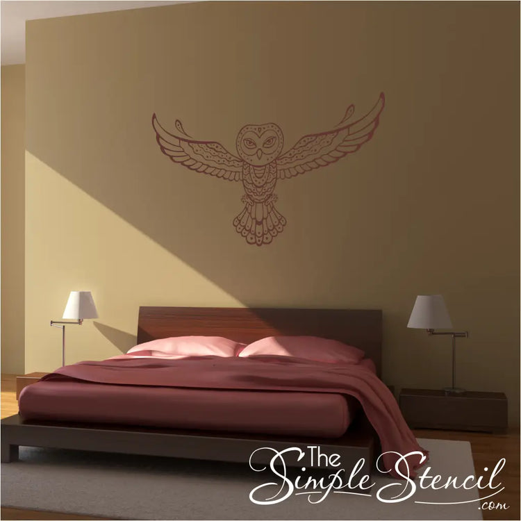A tribal owl vinyl wall decal in a reddish-brown color above a wooden bed in a modern, boho-style bedroom.