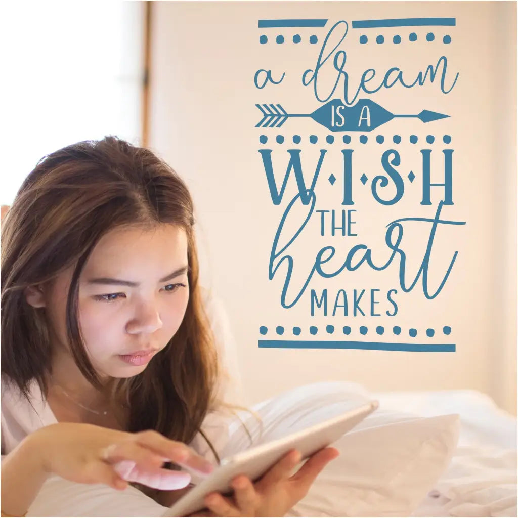 Whimsical wall quote decal for a little girl's room that reads: a dream is a wish the heart makes. Showing on a girl's room wall where she sits to read.