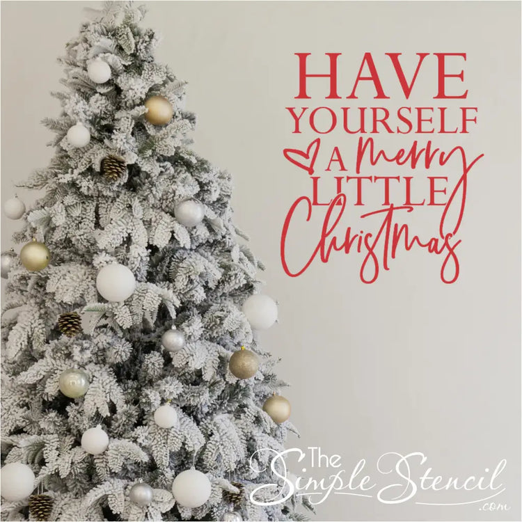 Red Christmas song lyrics vinyl decal reading 'Have Yourself a Merry Little Christmas' on a white wall next to a flocked Christmas tree. Features a bold and scripted font combination and a heart flourish; ideal nostalgic holiday decor.