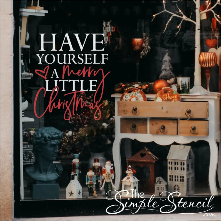 Red and white retail window display decal reading 'HAVE YOURSELF A merry LITTLE Christmas' on a store window filled with vintage holiday items. Excellent example of Christmas storefront decoration using a two-color vinyl graphic.