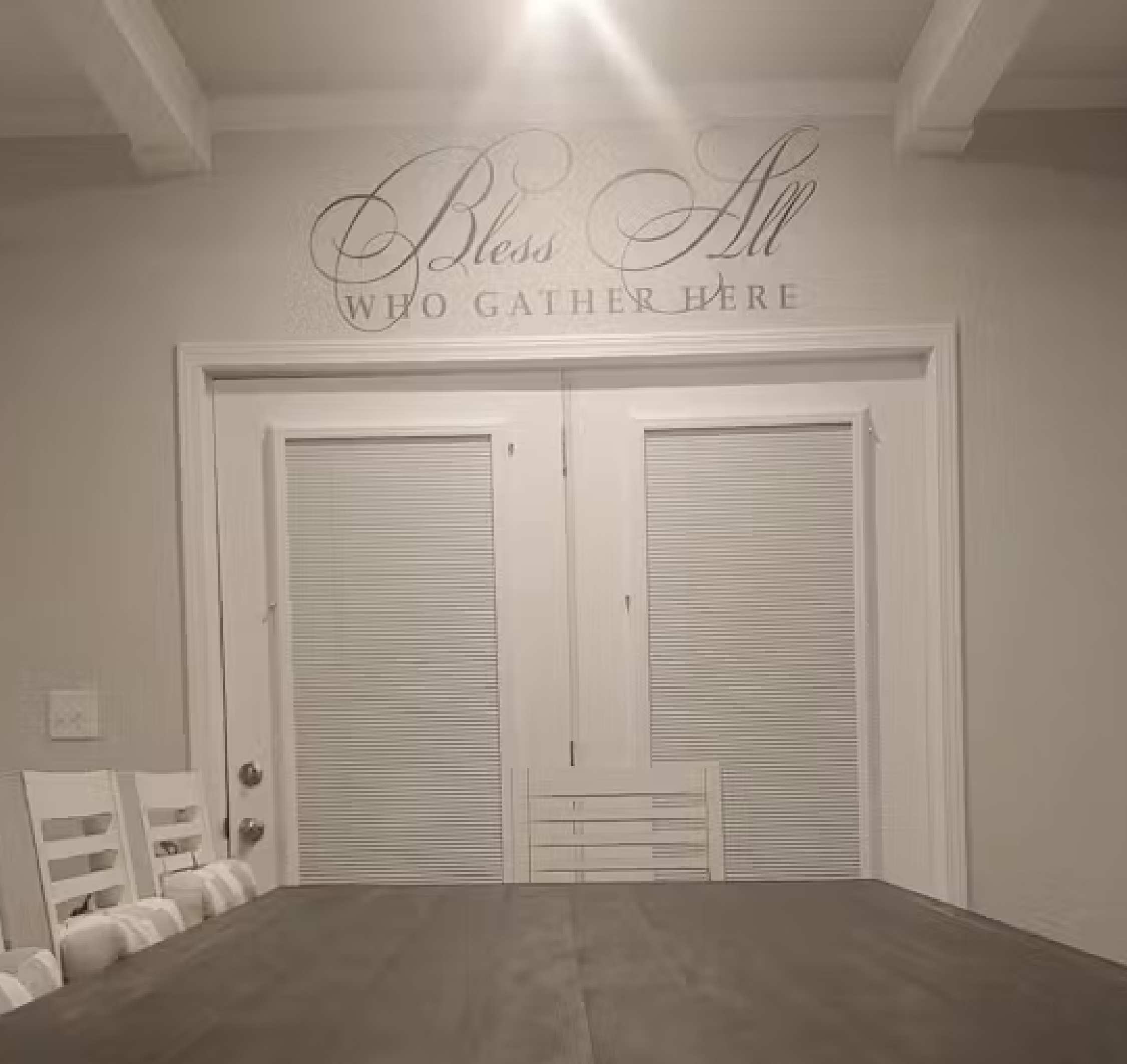 A picture of a customers dining room with their Simple Stencil wall decal displayed over the table that reads: Bless all who gather here in a beautiful way. By TheSimpleStencil.com