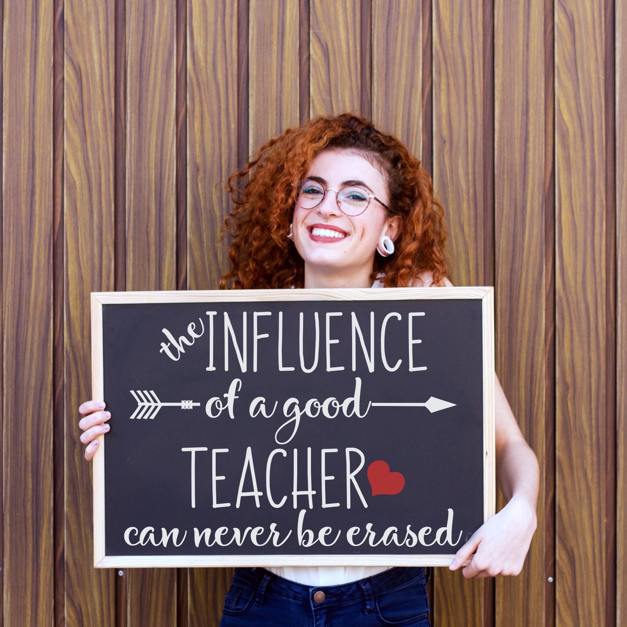 A happy teachers displaying a sign her students gifted her during teacher appreciation week that reads: The influence of a good teacher can never be erased. By TheSimpleStencil