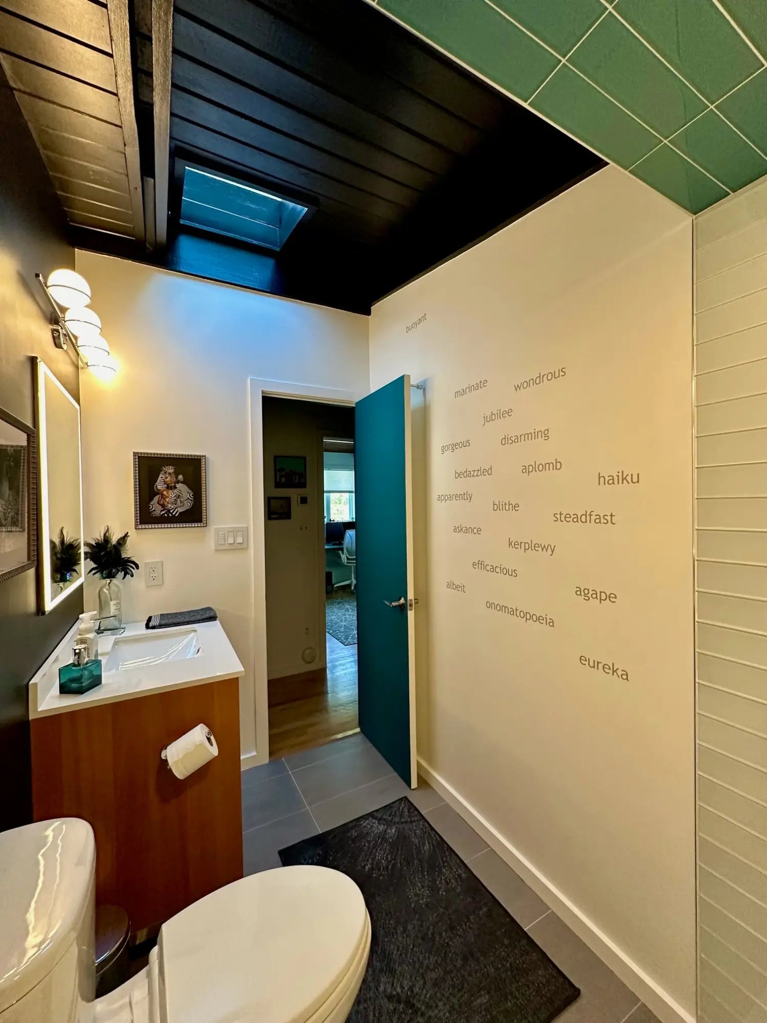  Close-up photo of a bright white bathroom wall with warm grey vinyl decals featuring a list of fun and quirky words in a scattered pattern. 