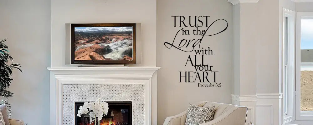 Proverbs 3:5 wall decal featuring 'Trust in the Lord with all your heart' in a mix of bold serif and elegant script fonts, displayed in a modern living room next to a white fireplace mantle