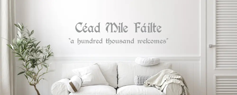A St. Patrick's Day and Irish Blessing decal collection, featuring the Gaelic greeting 'Céad Míle Fáilte' (a hundred thousand welcomes) in an elegant Celtic-style font, displayed on a clean white wall above a modern living room sofa.