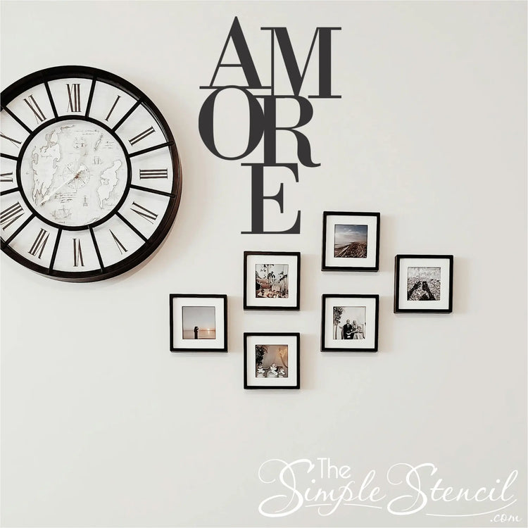 Matte Black  'AMORE' wall sticker incorporated into a living space gallery wall display, positioned next to a large round Roman numeral clock and six black-framed family photos.