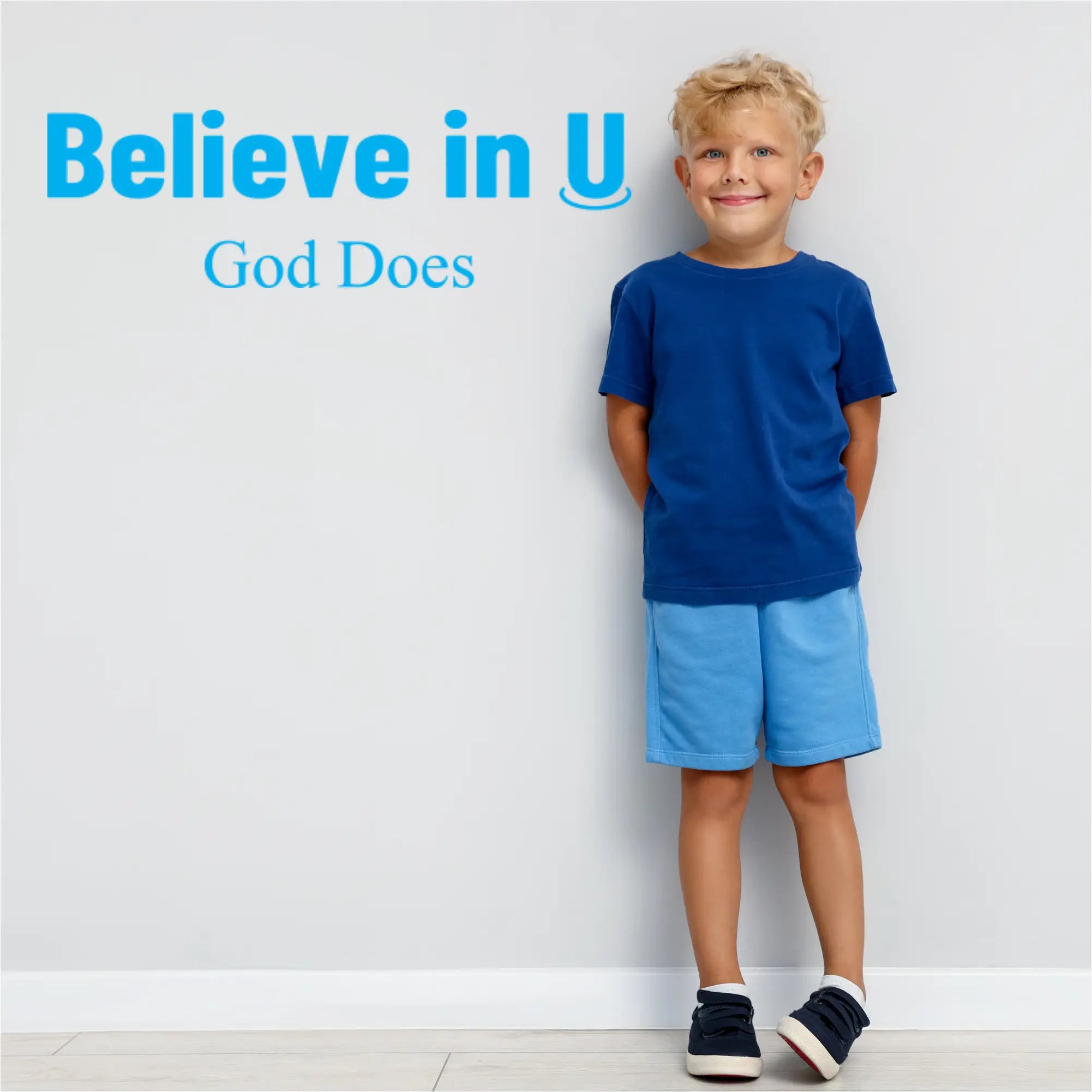 Wall decal on wall next to Child wearing a blue shirt and shorts with spiritual text that reads: Believe in U God does.