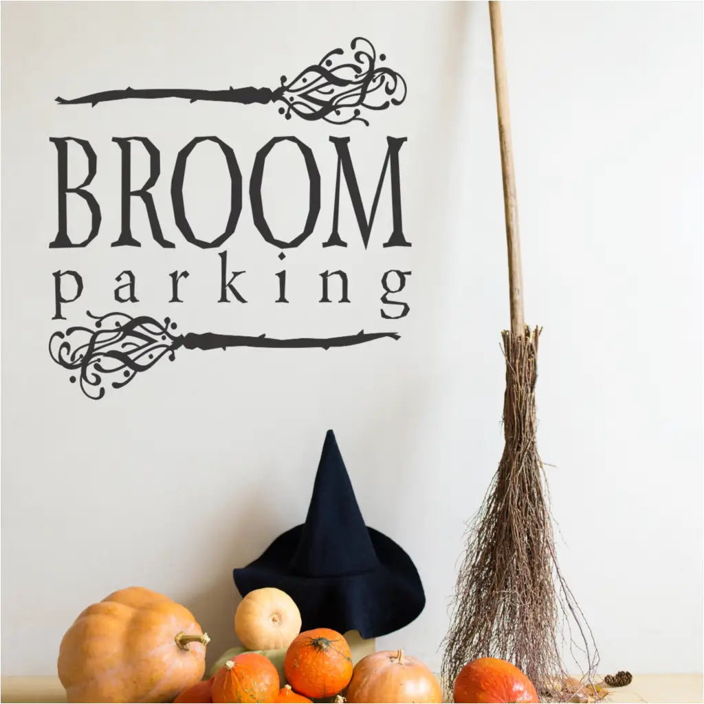 A black "Broom Parking" vinyl wall decal on a white wall, positioned above a witch's hat and a collection of pumpkins.