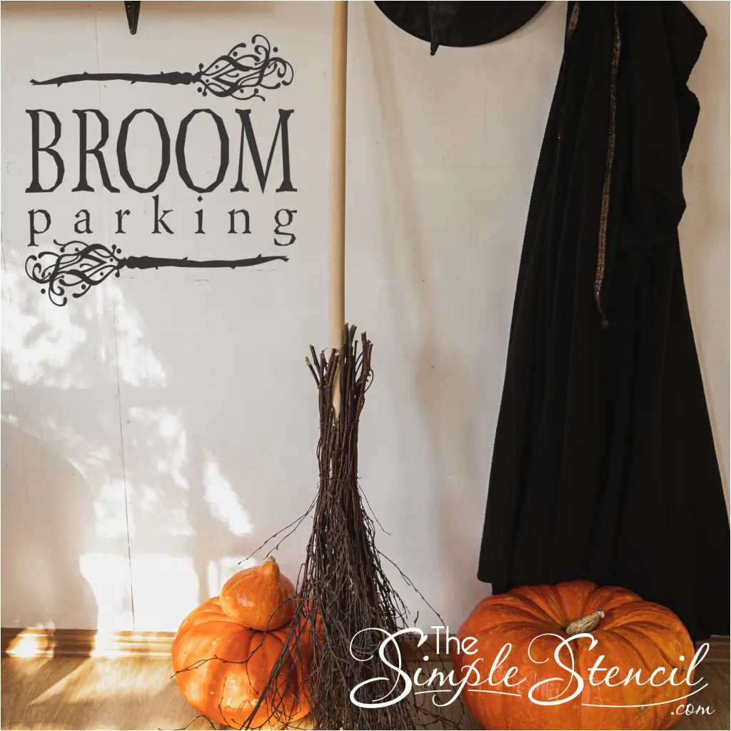 A black "Broom Parking" vinyl wall decal on a white wall, with a real broom, pumpkins, and a black robe nearby, creating a whimsical Halloween scene.