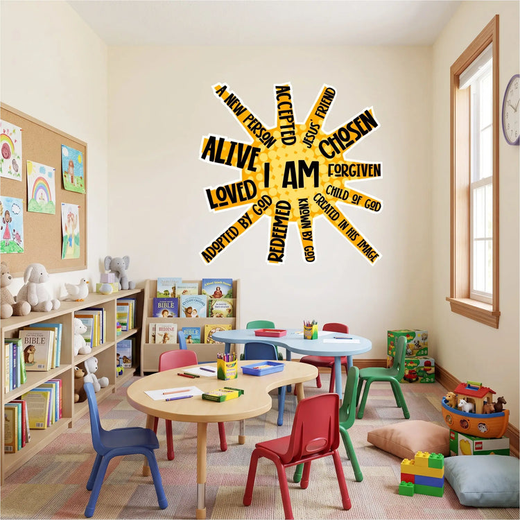 A church children's classroom or Sunday School room. The scene is viewed from a wide perspective, looking into a room with pale cream walls and a patterned carpet tile floor. Centered on the back wall is a large, yellow and black "I AM" sunburst wall decal with biblical phrases for kids. 