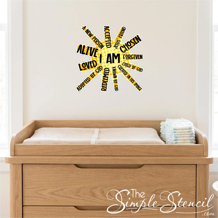 A high-resolution, square photograph focused on a light wood nursery changing table with a soft changing mat and neat stack of diapers in a church nursery. Directly above the changing table, affixed centrally to the light cream wall, is a single, perfectly rendered decal of the exact "I AM" sun-burst affirmation artwork from image_0.png. The decal is scaled appropriately as a small, focused accent piece. 