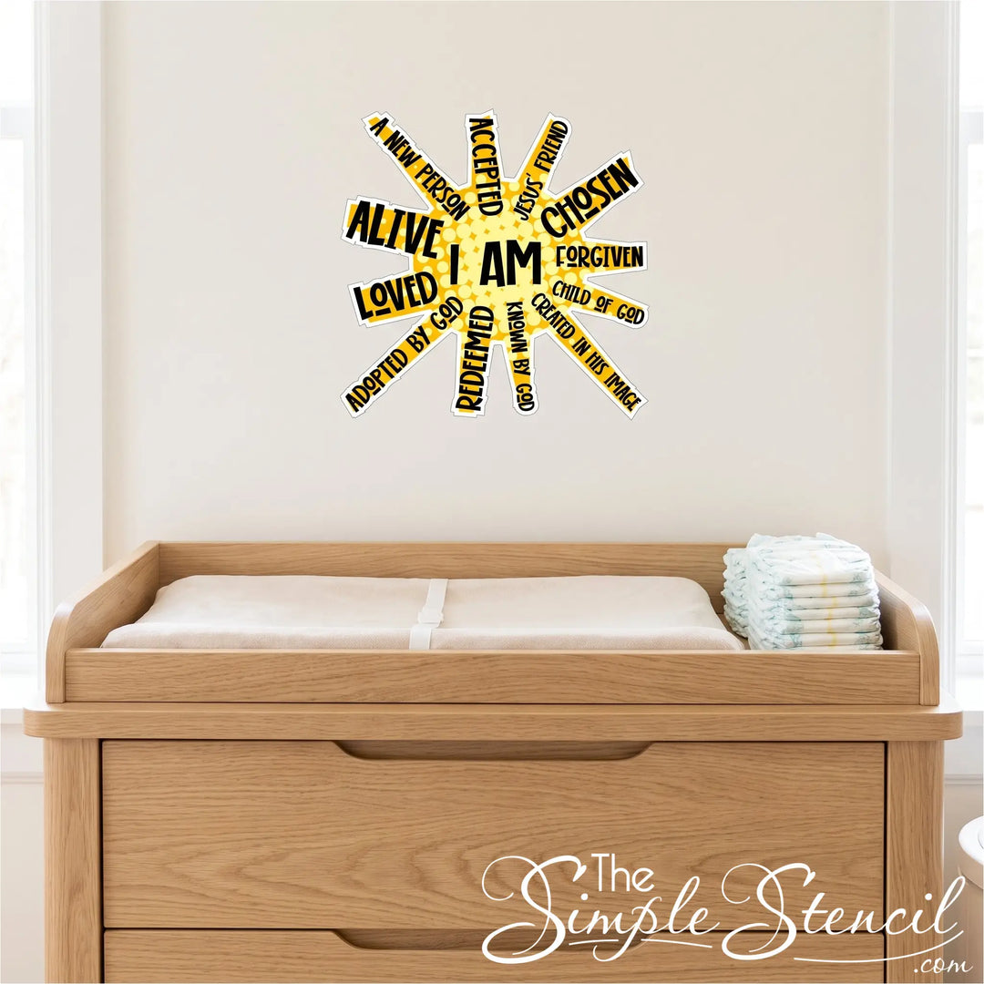 A high-resolution, square photograph focused on a light wood nursery changing table with a soft changing mat and neat stack of diapers in a church nursery. Directly above the changing table, affixed centrally to the light cream wall, is a single, perfectly rendered decal of the exact "I AM" sun-burst affirmation artwork from image_0.png. The decal is scaled appropriately as a small, focused accent piece. 