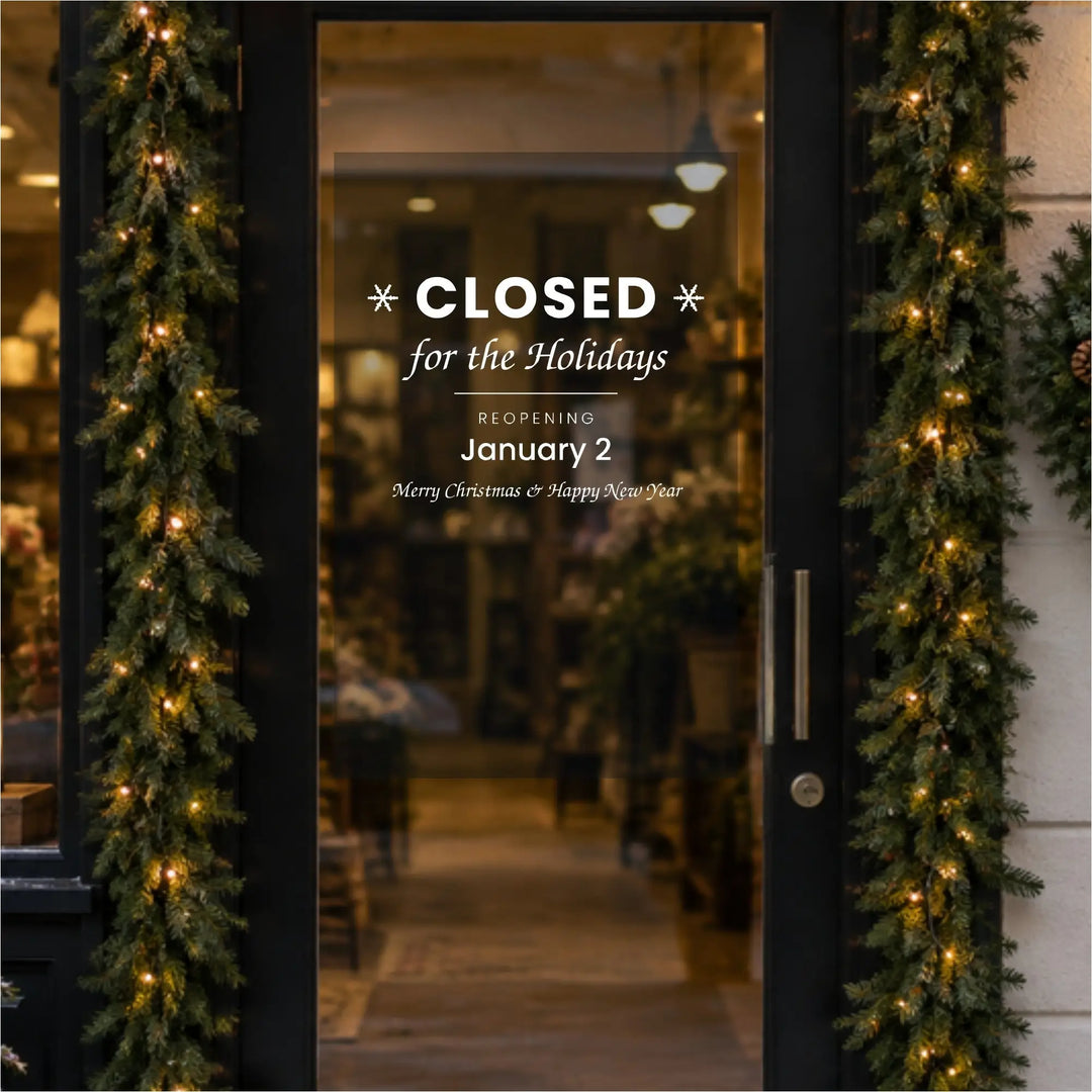 Closed for the Holidays decal with reopening date on a shop glass door decorated with Christmas garland