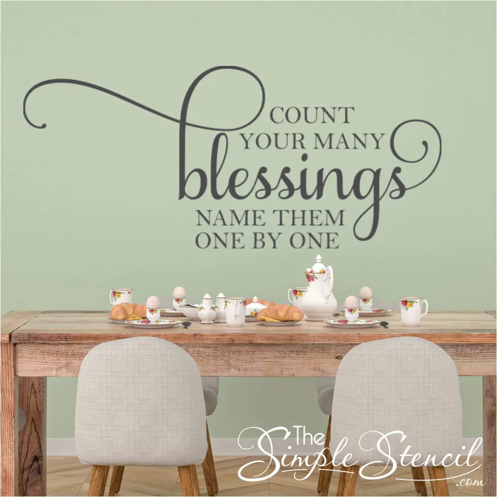 A beautifully scripted Count Your Many Blessings vinyl wall decal displayed on a dining room wall with a family gathered around the table. The decal is a reminder to be grateful for all the good things in our lives, and it is the perfect addition to any home.