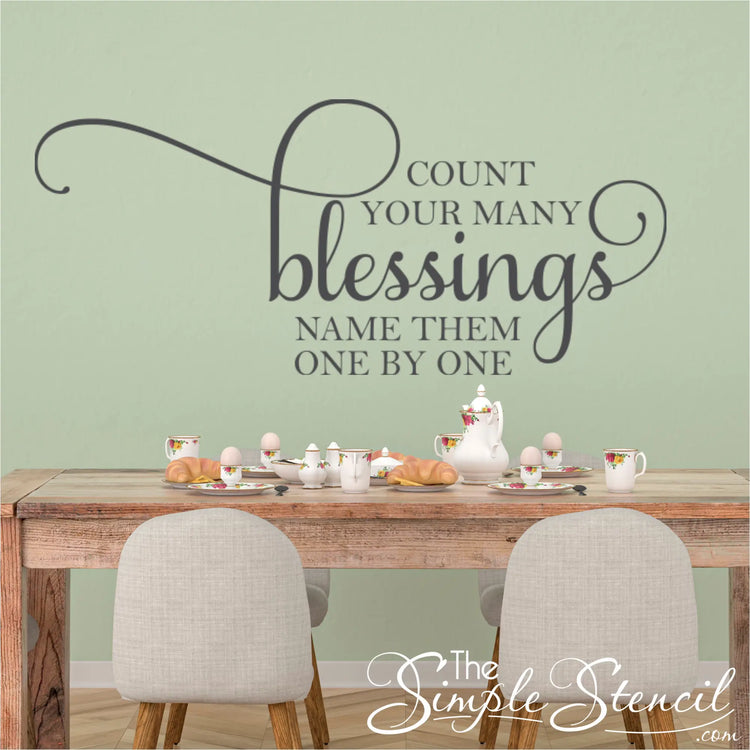 A beautifully scripted Count Your Many Blessings vinyl wall decal displayed on a dining room wall with a family gathered around the table. The decal is a reminder to be grateful for all the good things in our lives, and it is the perfect addition to any home.