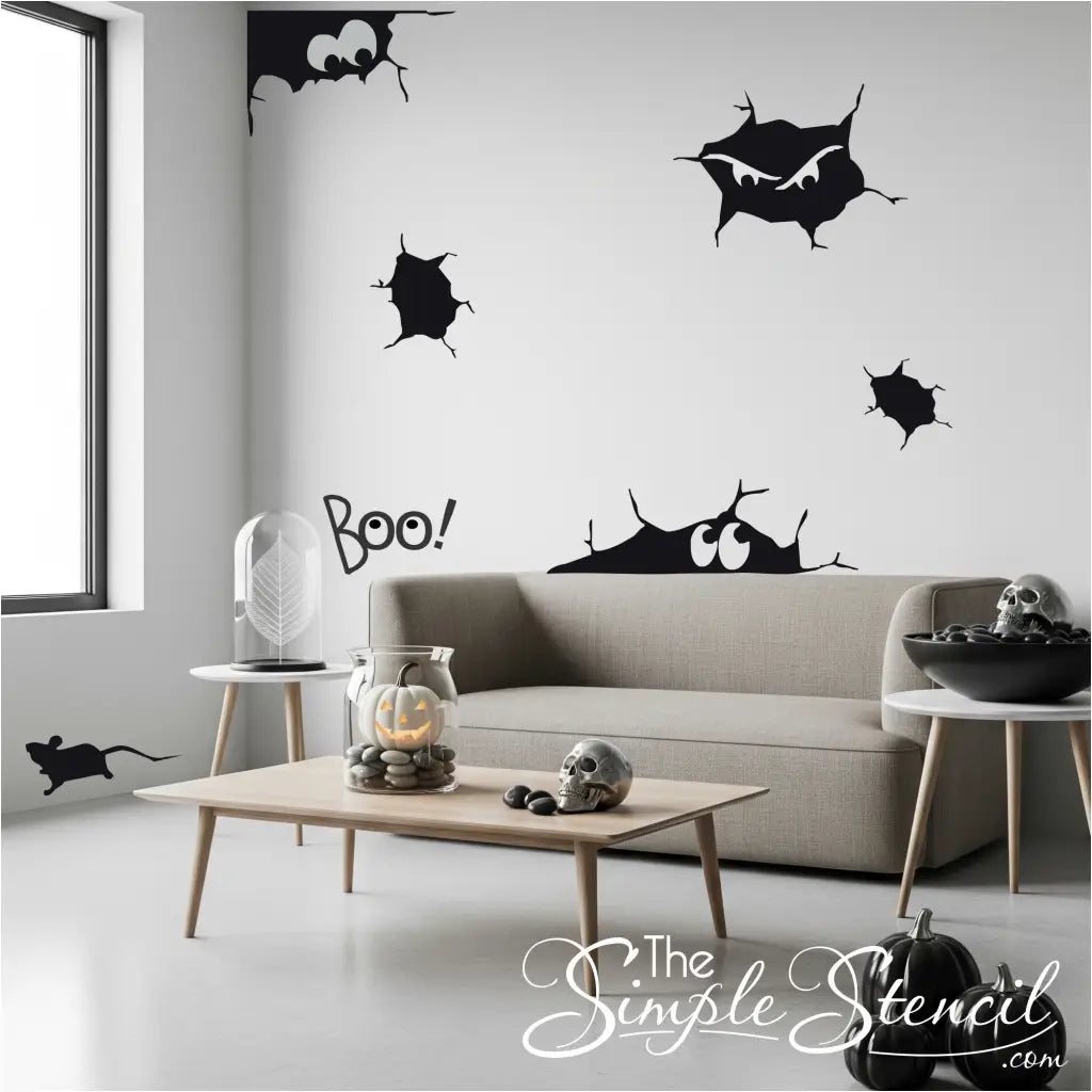 A gray living room wall with a black vinyl decal of spooky cracks and peering eyes, positioned above a couch with Halloween decor. The Simple Stencil decals shown in size large, color: matte black.