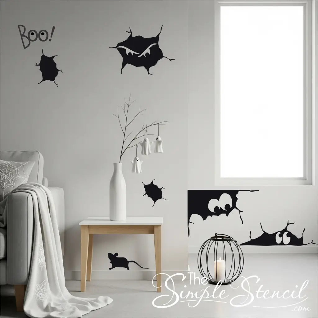 A living room decorated for Halloween with black vinyl wall decals of spooky cracks, peering eyes, and a rat on a light gray wall. The Simple Stencil decals shown in Large size in Matte Black