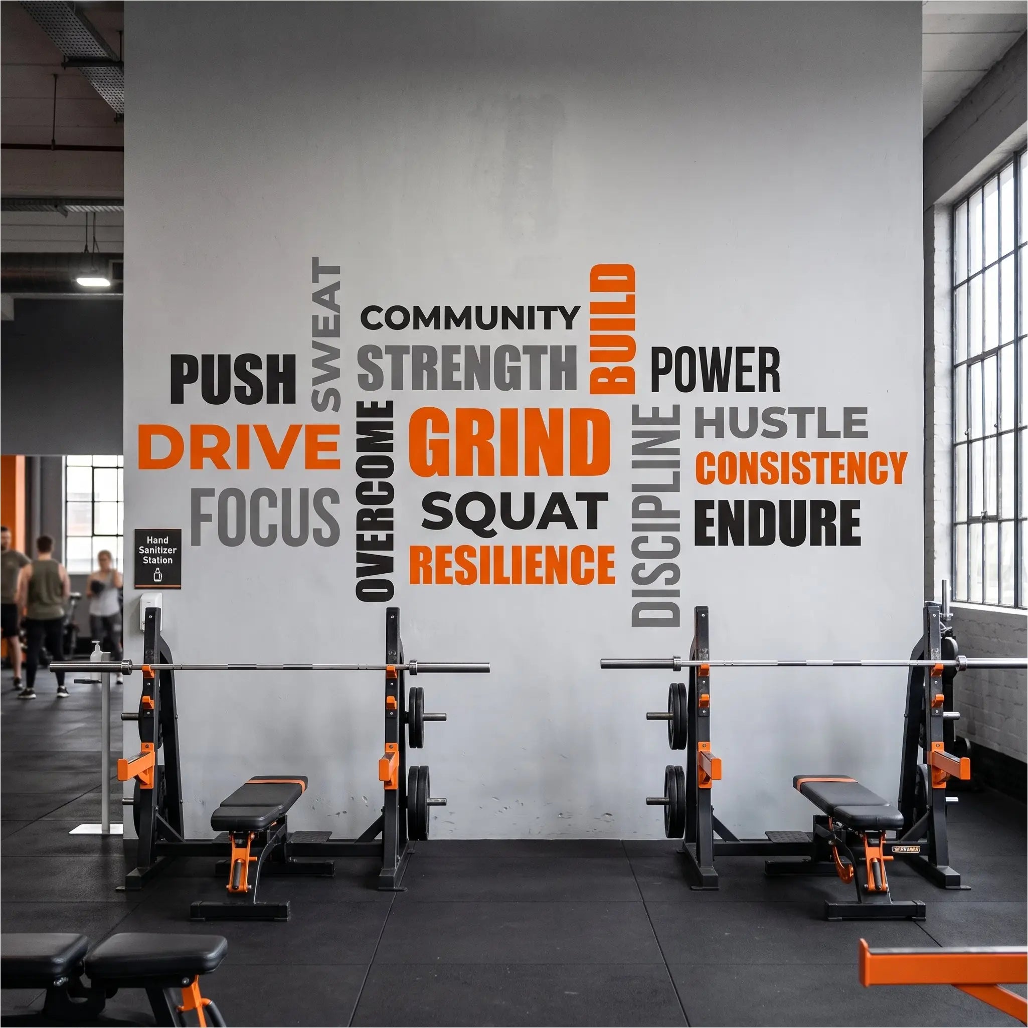 Large bright orange, grey, and black workout motivational word decal collage on a commercial gym wall mounted above weightlifting racks.