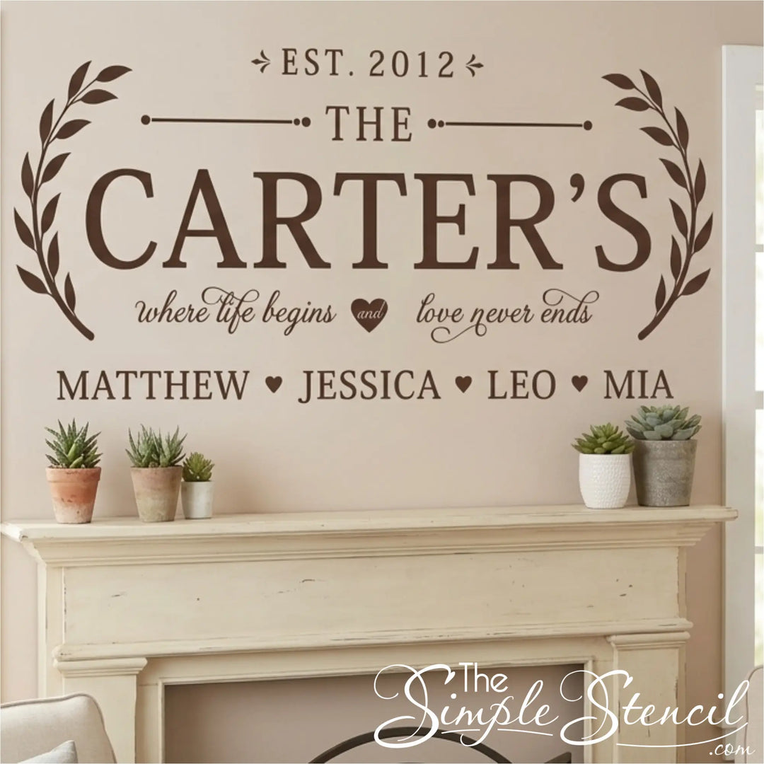Custom wall decal featuring the text 'THE CARTER'S' with decorative laurel wreaths, 'EST. 2012', and names 'MATTHEW', 'JESSICA', 'LEO', and 'MIA' below, displayed on a beige wall above a white fireplace mantel with small potted plants.