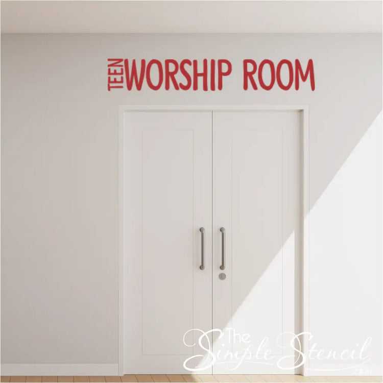 Red vinyl decal with the words "WORSHIP ROOM" mounted above a doorway leading to a church youth area. The doorway signage below reads "Teen Worship Room". (The Simple Stencil)