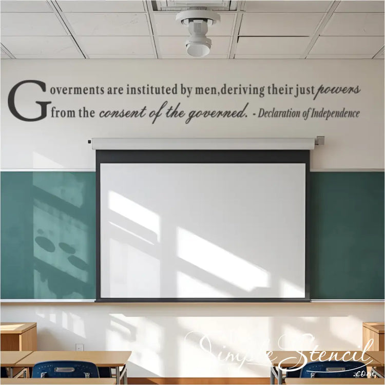 Gray wall decal of a quote from the Declaration of Independence, reading "Governments are instituted by men, deriving their just powers from the consent of the governed." The decal is installed above a blackboard and projection screen in a classroom.